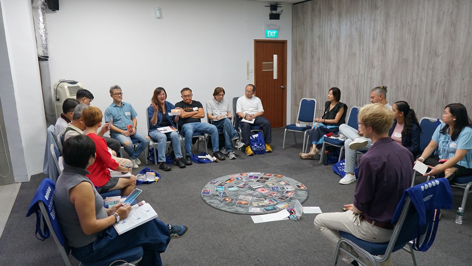 The group sits in a circle around a ring of picture cards on the floor, Singapore